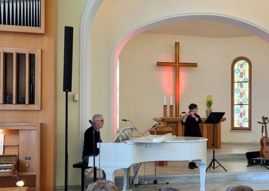 Ein Musiker am Klavier in einer Kirche mit einem Kreuz im Hintergrund.
