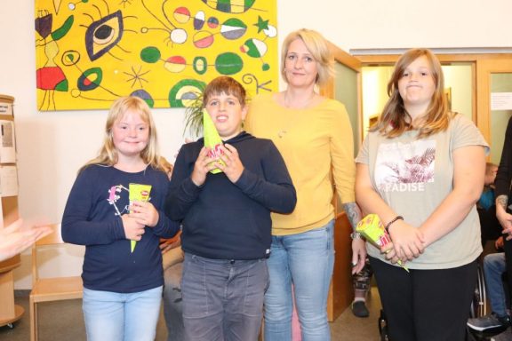 Gruppe von vier Personen lächelt, steht zusammen in einem hellen Raum.