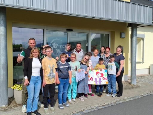 Gruppe von Kindern und Erwachsenen vor einem Gebäude, einige halten ein Plakat.