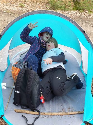 Zwei Kinder in einem Zelt, eines macht ein Peace-Zeichen, beide wirken entspannt.