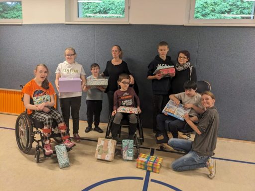 Eine Gruppe von Kindern und Erwachsenen, die Geschenke in einer Sporthalle halten.