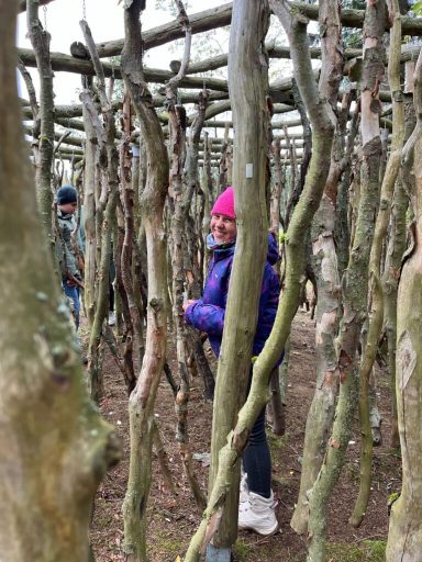 Ein Kind in einem lila Mantel und pinker Mütze steht zwischen verwundenen Ästen.