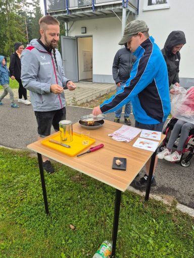 Personen an einem Tisch im Freien, eine Aktion mit einer Waage und Lebensmitteln.