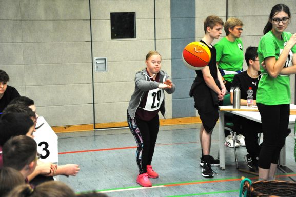 Mädchen in Sportkleidung wirft einen Basketball in einer Sporthalle.