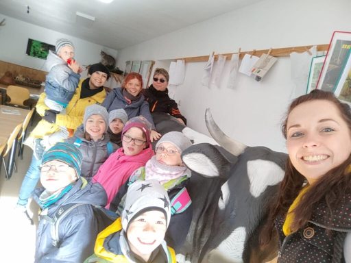 Eine Gruppe von Kindern und Erwachsenen sitzt zusammen in einem Raum mit Kuhskulpturen.