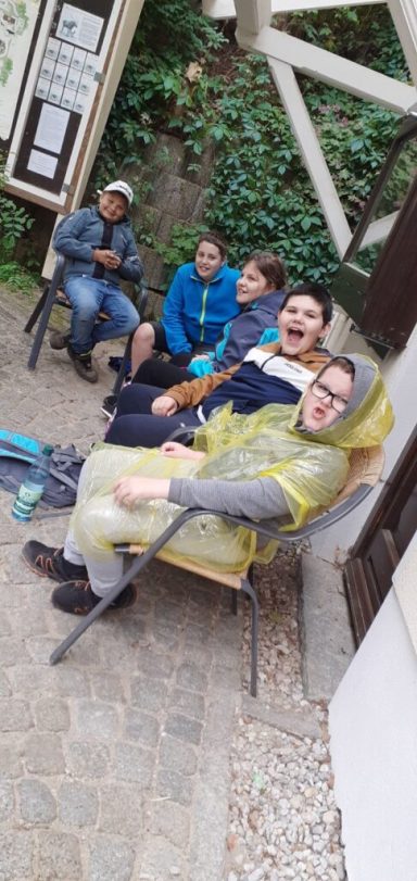 Fünf Personen sitzen entspannt auf Stühlen in einem grünen Außenbereich.