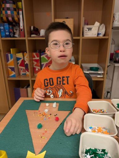Ein Kind mit Brille gestaltet einen Weihnachtsbaum aus bunten Materialien.