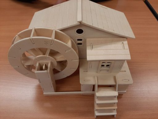 Modell eines Holzwasserrads neben einem kleinen Holzhaus auf einem Tisch.