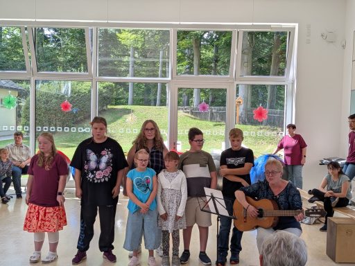Gruppe von Kindern und Erwachsenen bei einer Musikaufführung in einem hellen Raum.