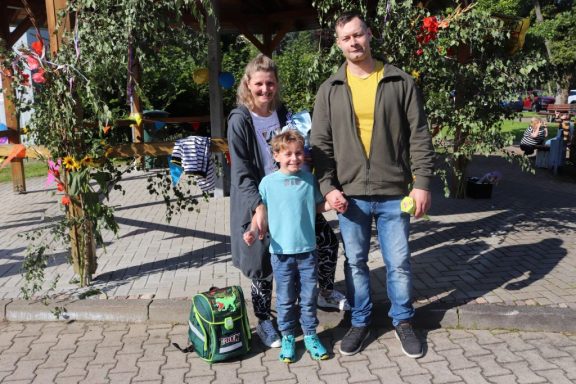 Familie steht zusammen im Freien, lächelnd, mit einem Kind in der Mitte.