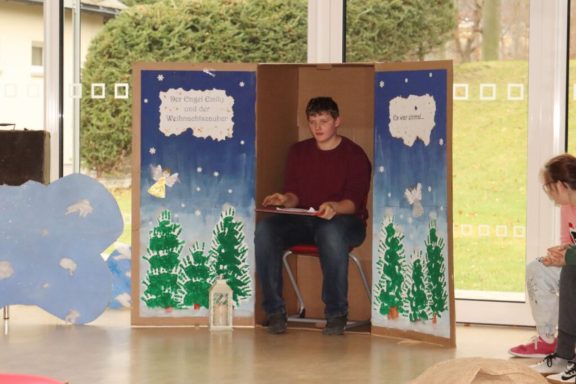 Junger Mann sitzt in einem dekorierten Raum, umgeben von bemalten Bäumen und Wolken.