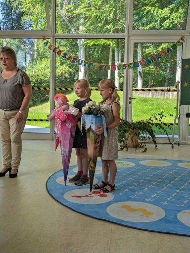 Drei Kinder halten große Eisbecher in einem hellen Raum mit grünen Pflanzen im Hintergrund.