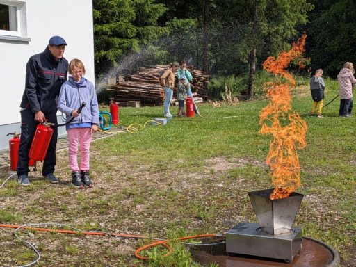 Kinder üben mit Feuerlöschern an einer kleinen Flamme im Freien.
