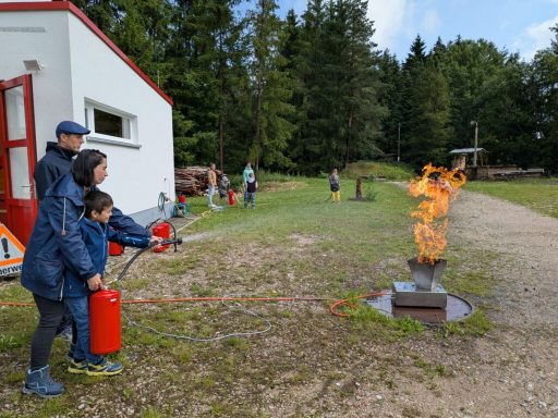 Personen üben den Umgang mit einem Feuerlöscher bei einer Brandschutzübung im Freien.