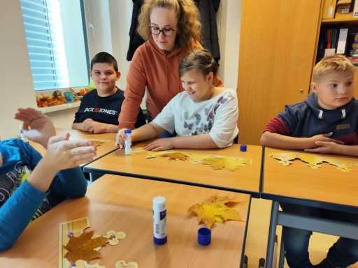 Kinder basteln mit einer Lehrerin, verwenden Farbe und Kleber auf Papiervorlagen.