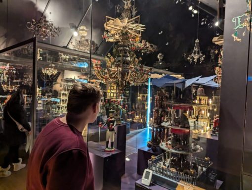 Person betrachtet eine Ausstellung mit kunstvollen, dekorativen Objekten in einem Museum.