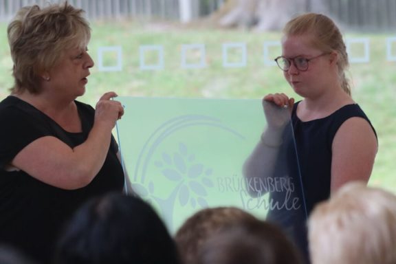 Zwei Frauen stehen nebeneinander, eine spricht, die andere schaut ernst.