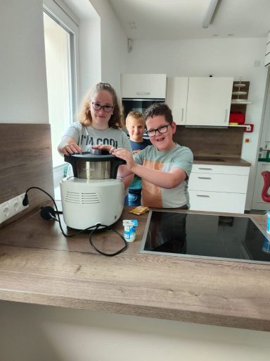 Drei Kinder stehen in einer Küche und bedienen einen Kochautomaten.