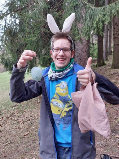 Ein Mann mit Hasenohren hält ein Osterei und gibt einen Daumen nach oben.