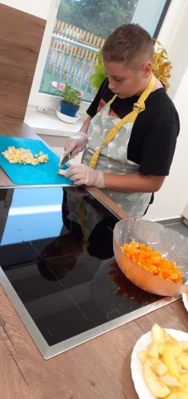 Ein Junge schneidet Gemüse auf einem blauen Schneidebrett in einer Küche.