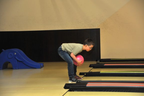 Ein Junge beugt sich, um einen pinken Bowlingball zu rollen.