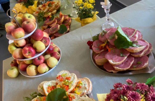 Vielfältige Obst- und Sandwichplatte mit Äpfeln, Aufschnitt und bunten Blumen.