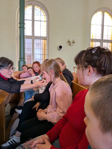 Jugendliche sitzen in einer Kirche, während jemand ihnen etwas erklärt oder zeigt.