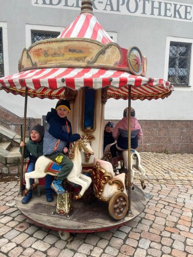 Kinder sitzen auf einem Karussell mit einem gestreiften Dach und Holzpferden.