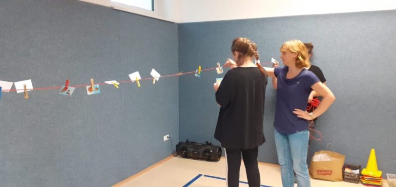 Zwei Personen in einem Raum, die an einer bunten Schnur mit Wäscheklammern arbeiten.