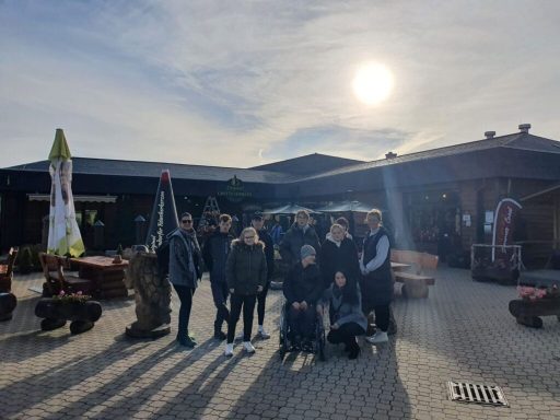 Gruppe von Menschen vor einem Gebäude bei sonnigem Wetter.