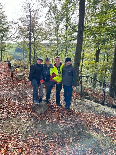 Vier Personen in einem Herbstwald, umgeben von Bäumen und fallenem Laub.