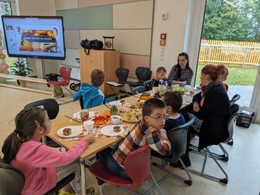 Eine Gruppe von Kindern und Erwachsenen sitzt an einem Tisch beim Essen und Reden.