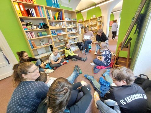 Gruppensitzung von Kindern und Erwachsenen in einem farbenfrohen Leseraum.