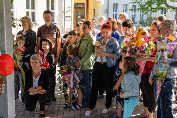 Eine Gruppe von Menschen, darunter Kinder und Erwachsene, hält Blumensträuße und lächelt.