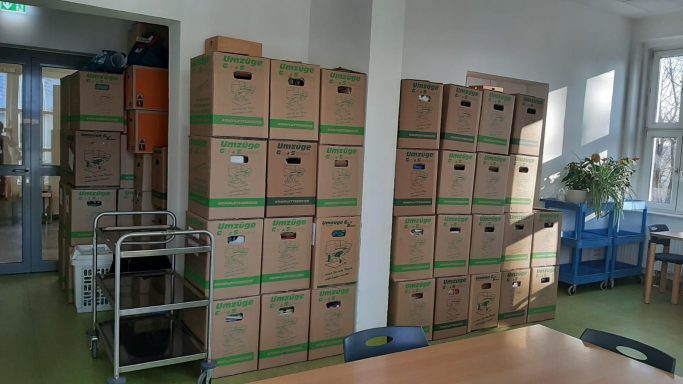 Kartonagen in einer Lagerumgebung, gestapelt und organisiert, mit einem Tisch im Vordergrund.