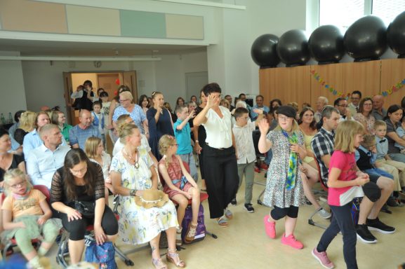 Menschenmenge in einem Raum, darunter Kinder und Erwachsene, in festlicher Atmosphäre.