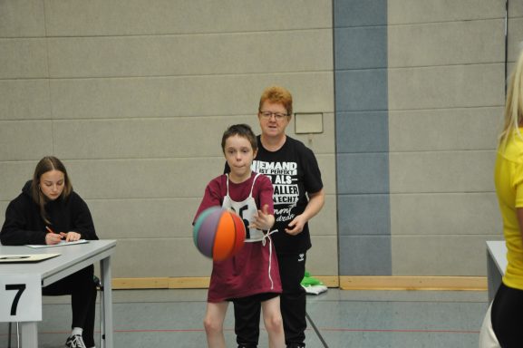 Ein Junge mit Basketball, während eine Frau im Hintergrund assistiert.