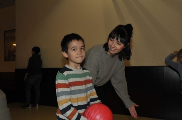 Ein Junge mit gestreiftem Pullover sitzt, während ein Mädchen hinter ihm lächelt und gestikuliert.