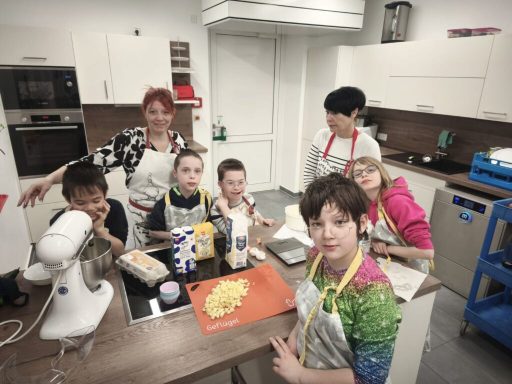 Eine Gruppe von Kindern und Erwachsenen in einer modernen Küche beim Backen.