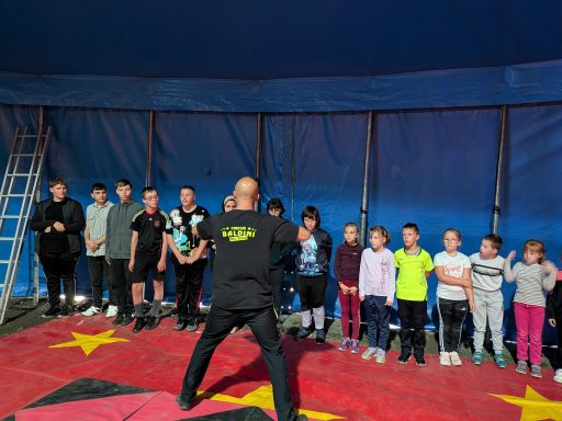 Zirkustraining für Kinder mit einem Trainer und mehreren Teilnehmern in einem Zelt.