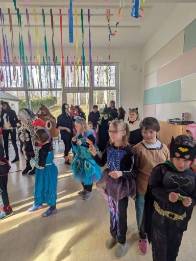 Kinder in Kostümen stehen in einer bunten, festlich dekorierten Umgebung.