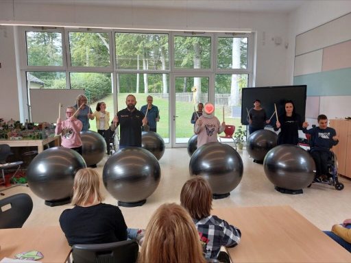 Gruppentraining mit großen Schwarzbällen in einem hellen Raum, Teilnehmer stehen und sitzen.