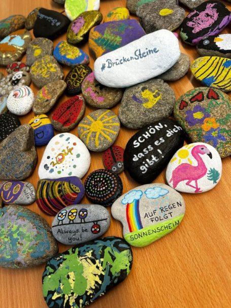 Bunte bemalte Steine in verschiedenen Formen und Designs auf einem Holztisch.