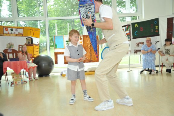 Ein Junge in grauen Shorts steht neben einem Erwachsenen, während andere zuschauen.