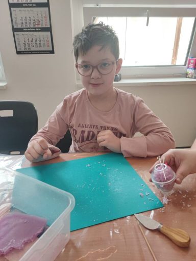 Ein Kind mit Brille sitzt an einem Tisch, umgeben von Bastelmaterialien.