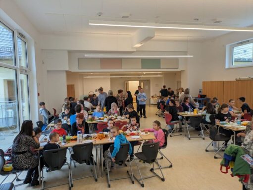 Viele Kinder und Erwachsene sitzen an Tischen und arbeiten gemeinsam an Aktivitäten.