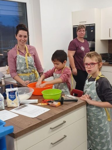 Drei Personen in einer Küche, die zusammen Kochen und Backen, mit Zutaten und Utensilien.