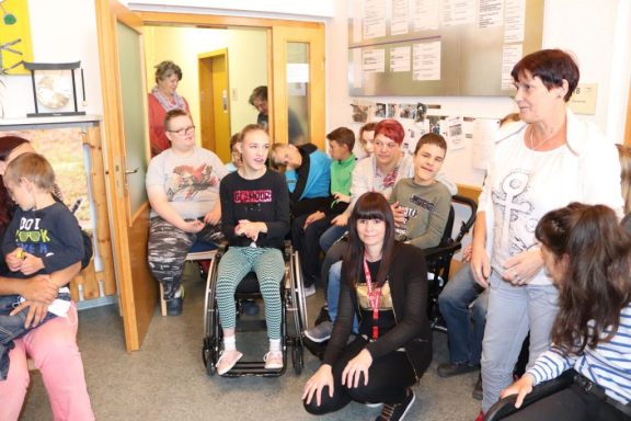 Gruppensitzung mit Kindern und Erwachsenen in einem Raum, einige sitzen im Rollstuhl.