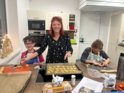 Frau mit rotem Haar backt mit zwei Kindern Plätzchen in einer modernen Küche.
