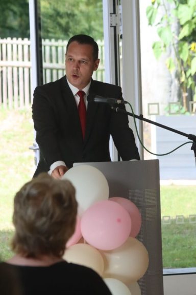 Mann in Anzug spricht am Rednerpult, im Hintergrund Ballons und Publikum.